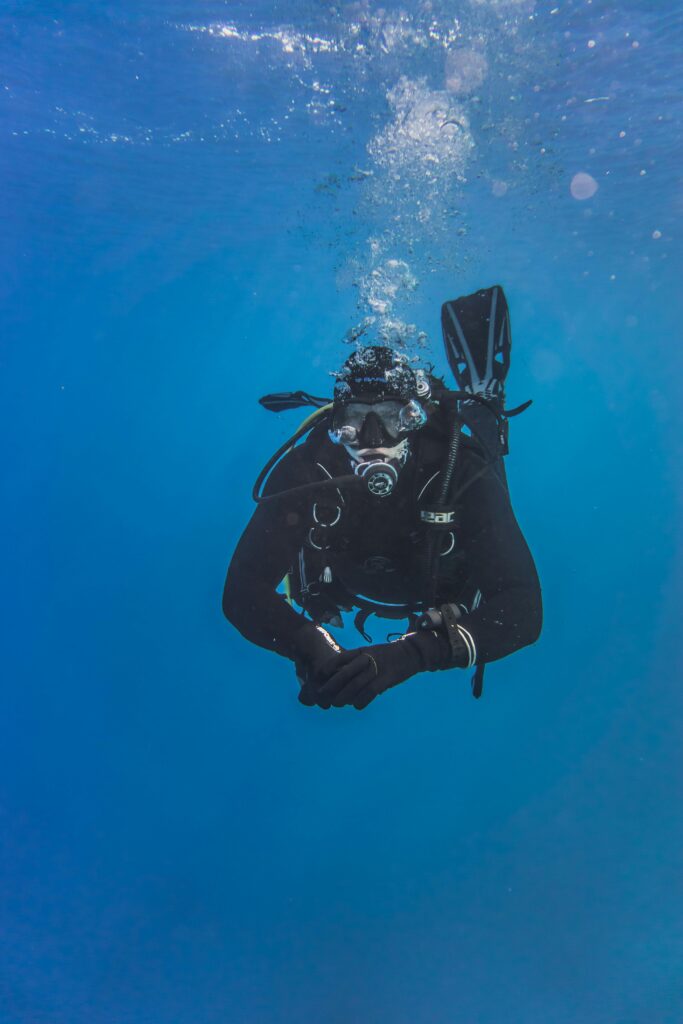 A scuba diver is slowing descending into the water. The surface is visible. He is peaceful. 