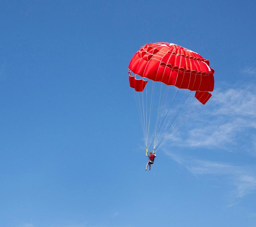 Person under red parachute canopy in mid air while skydiving in Cambodia