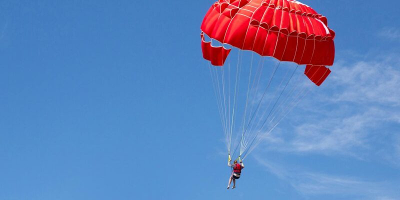 Person under red parachute canopy in mid air while skydiving in Cambodia